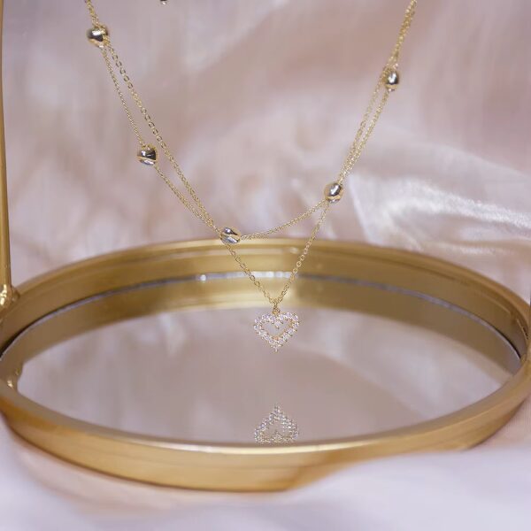 a gold chain necklace with a heart shaped pendant on a gold plate