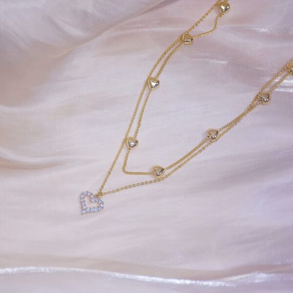 a gold chain necklace with a heart pendant on a white fabric